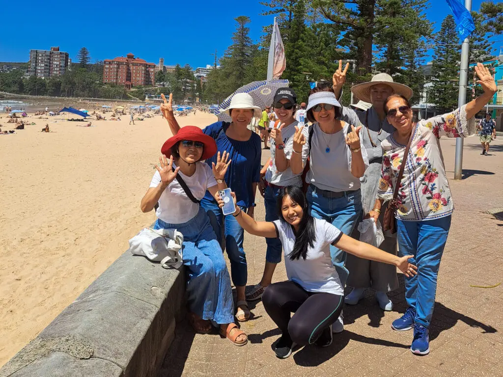 Group of people standing on Manly Beach with ocean waves and blue sky in the background.