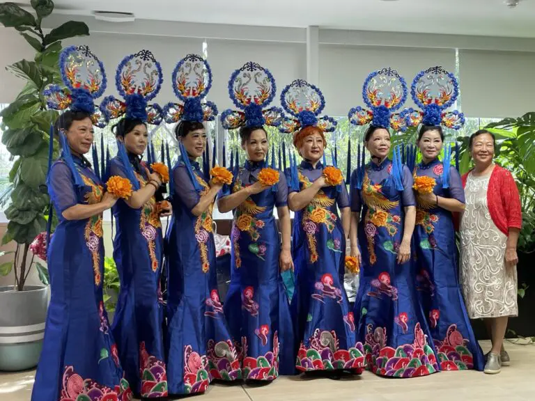 Women in traditional blue attire perform at a cultural event supported by Metro Assist.