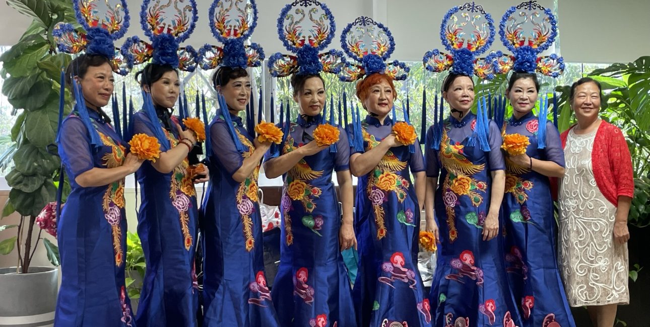 Women in traditional blue attire perform at a cultural event supported by Metro Assist.